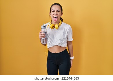 Young south asian woman wearing sportswear drinking water sticking tongue out happy with funny expression. emotion concept.  - Shutterstock ID 2215444363
