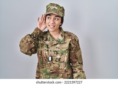 Young South Asian Woman Wearing Camouflage Army Uniform Smiling With Hand Over Ear Listening An Hearing To Rumor Or Gossip. Deafness Concept. 