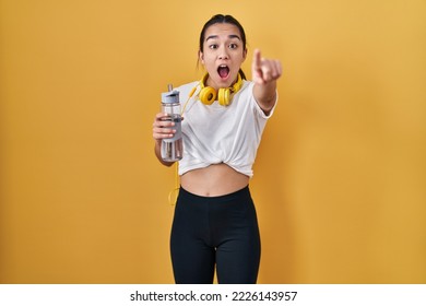Young south asian woman wearing sportswear drinking water pointing with finger surprised ahead, open mouth amazed expression, something on the front  - Shutterstock ID 2226143957