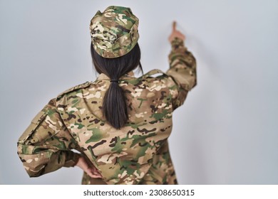 Young south asian woman wearing camouflage army uniform posing backwards pointing ahead with finger hand 