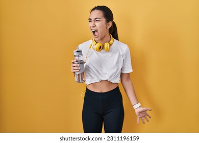 Young south asian woman wearing sportswear drinking water angry and mad screaming frustrated and furious, shouting with anger. rage and aggressive concept.  - Shutterstock ID 2311196159