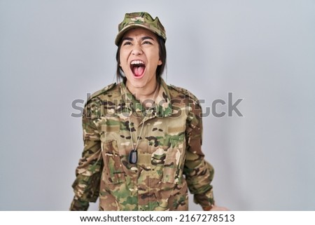 Young south asian woman wearing camouflage army uniform angry and mad screaming frustrated and furious, shouting with anger. rage and aggressive concept. 