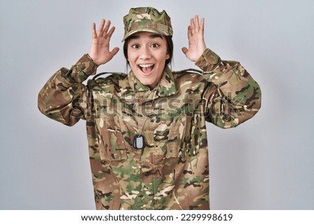 Young south asian woman wearing camouflage army uniform celebrating crazy and amazed for success with arms raised and open eyes screaming excited. winner concept 