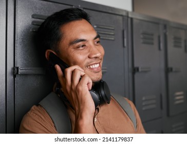 A Young South East Asian Man Talks On The Phone In Front Of Campus Lockers