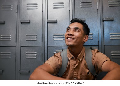 A Young South East Asian Student Sits In Front Of Campus Lockers Smiling