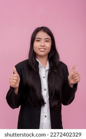 A young southeast asian female employee in a black jacket with arms crossed. Isolated on a light pink background. - Shutterstock ID 2272402329