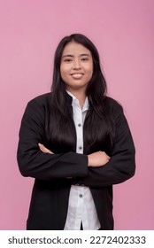 A young southeast asian female employee in a black jacket with arms crossed. Isolated on a light pink background. - Shutterstock ID 2272402333