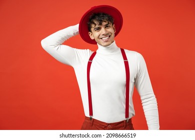 Young Spanish Latinos Attractive Smiling Happy Stylish Fashionable European Man 20s Wearing Casual White Shirt Trousers With Suspenders Touching Hat Isolated On Red Color Background Studio Portrait