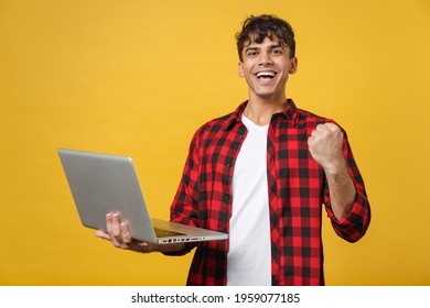 Young Spanish Latinos Excited Gladden Handsome Fashionable Friendly Man 20s In Red Checkered Shirt Hold Laptop Pc Computer Do Winner Gesture Clench Fist Isolated On Yellow Background Studio Portrait