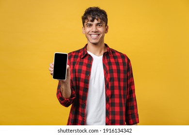 Young Spanish Latinos Smiling Handsome Cheerful Happyfashionable Man 20s In Red Checkered Shirt Holding Mobile Cell Phone With Blank Screen Workspace Area Isolated On Yellow Background Studio Portrait