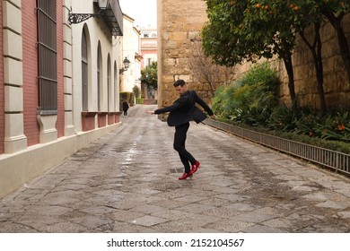 Young Spanish Man, Wearing Black Shirt, Jacket And Pants, With Red Dancing Shoes, Dancing Flamenco In The Street. Typical Spanish Concept, Art, Dance, Culture, Tradition.