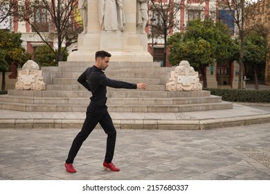 Young Spanish Man, Wearing Black Shirt And Pants, With Red Dancing Shoes, Dancing Flamenco In The Street. Typical Spanish Concept, Art, Dance, Culture, Tradition.