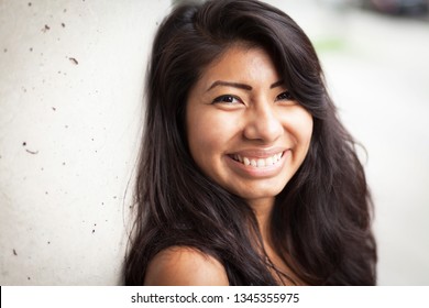Young Spanish woman smiling at the camera. She is leaning against a wall - Shutterstock ID 1345355975