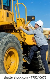 Young Specialist Is Getting Up To Yellow Forklift Operator Cabine Holding Handrails. Safety Glasses And White Hard Hat. 