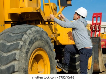 Young Specialist Is Getting Up To Yellow Forklift Operator Cabine Holding Handrails. Safety Glasses And White Hard Hat. 