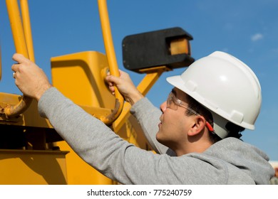 Young Specialist Is Getting Up To Yellow Forklift Operator Cabine Holding Handrails. Safety Glasses And White Hard Hat. 