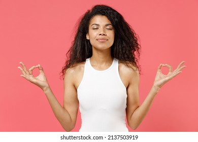 Young spiritual african american woman 20s wear casual white tank shirt hold spreading hands in yoga om gesture relax meditate try to calm down isolated on pink background. People lifestyle concept.
