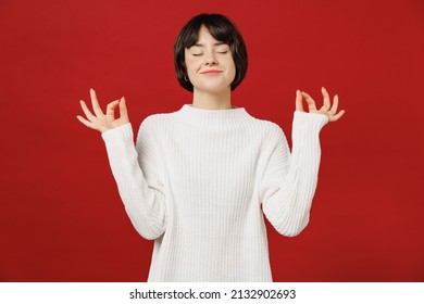 Young spiritual tranquil fun woman 20s wear white knitted sweater hold spreading hands in yoga om aum gesture relax meditate try to calm down isolated on plain red color background studio portrait.