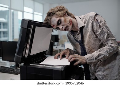 Young Spooky Businessman With Zombie Greasepaint On Face And Hands Bending Over Xerox Machine