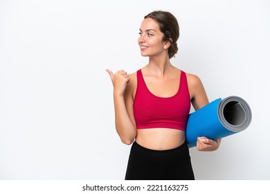 Young sport caucasian woman going to yoga classes while holding a mat isolated on white background pointing to the side to present a product