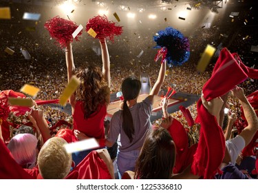 Young Sport Supporter Happy Fans At Basketball Arena. Two Beautiful Women With Red And Blue Pompoms Support The Basketball Team During The Game