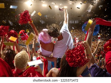 Young Sport Supporter Happy Fans At Basketball Arena. Beautiful Woman In A Pink Wig And Man Couple Hugging, Making Selfie Photo And Support The Basketball Team During The Game