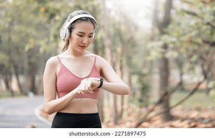 Young sport Woman with wireless headphone using smartwatch Checks Activity Tracker During Outdoor Exercise. - Powered by Shutterstock