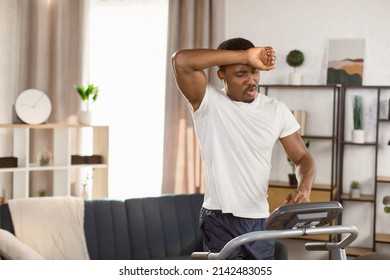 Young sportive African American man shorts and a white t-shirt trainig at home, doing cardio exercies on a treadmill while wipes sweat from his forehead. Concept of sport health action nutrition - Powered by Shutterstock