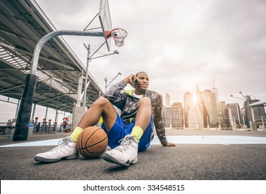Young sportive afroamerican man sitting on a basketball court and talking at phone - Basketball player calling his friends to organize a match