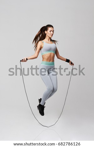 Young sportive beautiful girl doing exercises with jumping rope over white background.