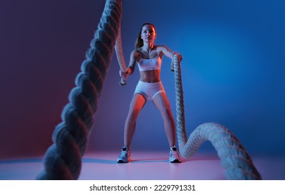 Young sportive girl training and sports equipment  ropes isolated over gradient blue purple background in neon light  Power  Modern sport  motion  youth concept  Fitness  hobby  healthy lifestyle
