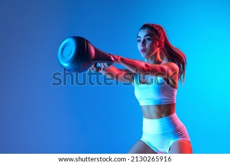 Young sportive girl training with sports equipment isolated on gradient blue-pink studio background in neon light. Modern sport, action, motion, youth concept. Fitness, hobby, healthy lifestyle