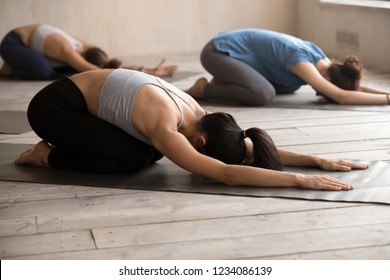 Young sportive girls practising together yoga positions at group session. Slim women lying resting on rubber mats doing Child Pose, calming the body, mind and spirit, stimulates the third eye point