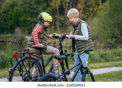 Young Sportive Slim Short Haired Randmother Teaches Her Grandson How To Ride A Bike At Nature. Different Generation Family Communication Concept.