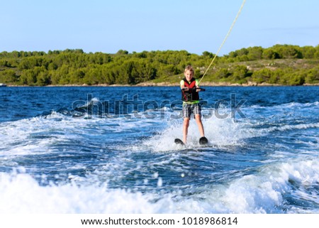 Young sportive teenage boy waterskiing from the boat. Adventurous summer holidays at the sea. Water sport activity on the beach.