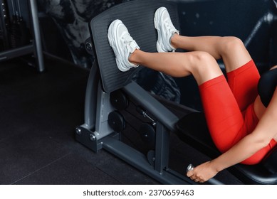 Young sportive woman in black bra, red shorts and white sneakers training legs on press simulator. Strong female workout regularly at sport club, close up. - Powered by Shutterstock