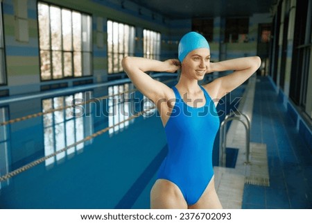 Young sportive woman in swimsuit putting on swimming hat