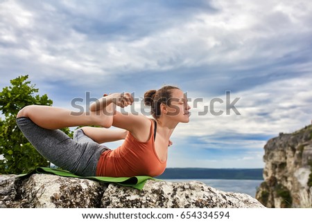 Young sportive woman training yoga on rock against beautiful big river.