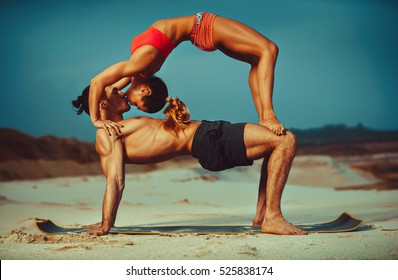 Young sports couple doing acroyoga exercises on sand beach and kissing