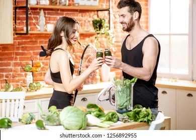 Young sports couple having a snack with vegetarian food drinking smoothie standing with rackets on the kitchen at home - Powered by Shutterstock