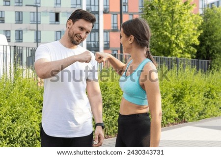 A young sports couple stand outdoors in a modern residential area with colorful buildings and parkland on a summer morning and happy with a successful jogging. The concept of physical training as a