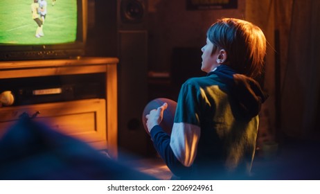 Young Sports Fan Watches American Football Match On TV At Home. Handsome Boy Supporting His Favorite Team. Holding A Football In Excitement. Nostalgic And Retro Childhood Concept.