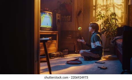 Young Sports Fan Watches A Tennis Match On TV At Home. Handsome Boy Supporting His Favorite Player, Nervously Holding A Green Tennis Ball. Nostalgic Retro Childhood Concept.