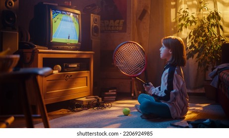 Young Sports Fan Watches A Tennis Match On TV At Home. Curious Girl Supporting Her Favorite Player, Imitating The Game With Her Racket. Nostalgic Retro Childhood Concept.