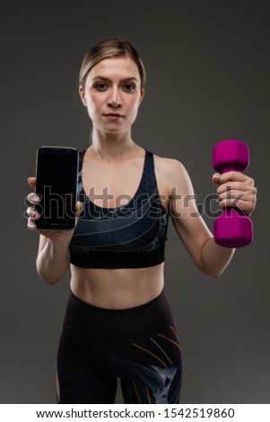 Young sports girl with long blonde hair stuffed in tail, beautiful appearance, sports body, in black top and legines, holds purple rubber gants and phone in her hands