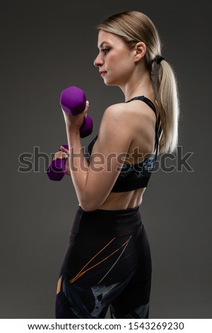 Young sports girl with long blonde hair stuffed in tail, beautiful appearance, sports body, in black top and legines, holds purple rubber gants in her hands