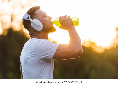 Young sports man drinking energy water from a bottle while resting after a run or workout in a summer park. Healthy lifestyle and wellbeing. A fit man drinks nutrition juice recovery after exercise. - Powered by Shutterstock