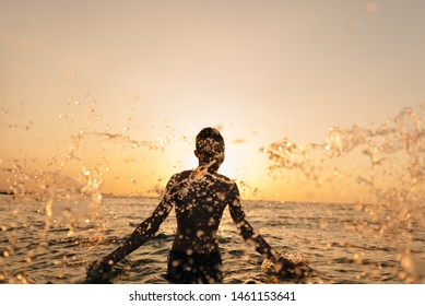 A young sports man guy rejoices at dawn and scatters around him a lot of spray. ocean at sunrise. - Shutterstock ID 1461153641