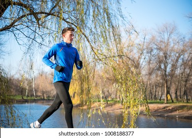 Young Sports Man Running in the Park in Cold Sunny Autumn Morning. Healthy Lifestyle and Active Sport Concept.