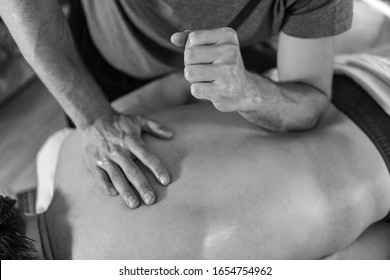 A Young Sports Massage Therapist Applying Pressure With The Elbow. Therapeutic Body Massage Treatment. Black And White Toned Image